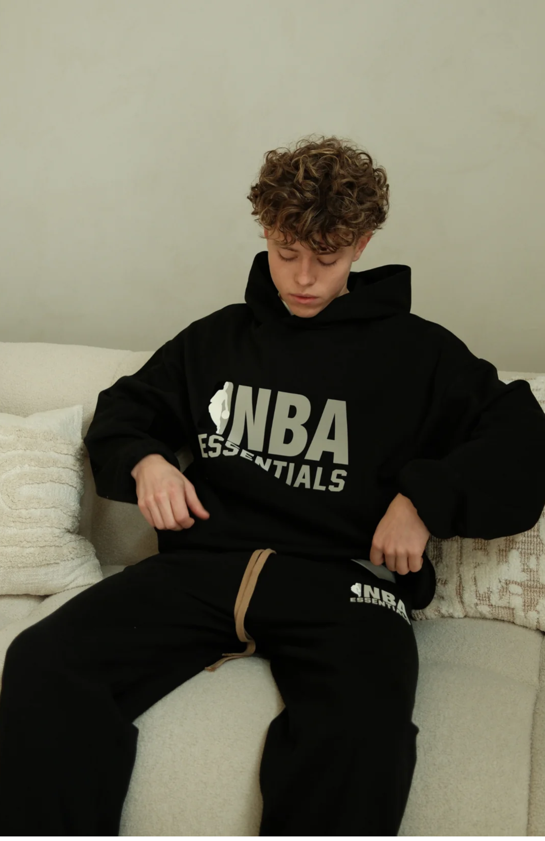 Fear Of God Essentials NBA hoodie in black while sitting